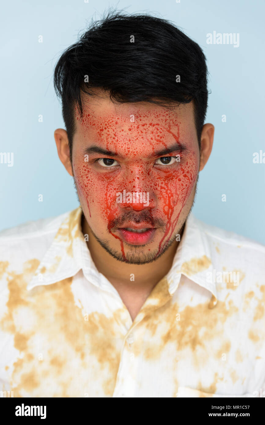 Volto del giovane pazzo uomo asiatico guardando la fotocamera con il sangue su di fa Foto Stock