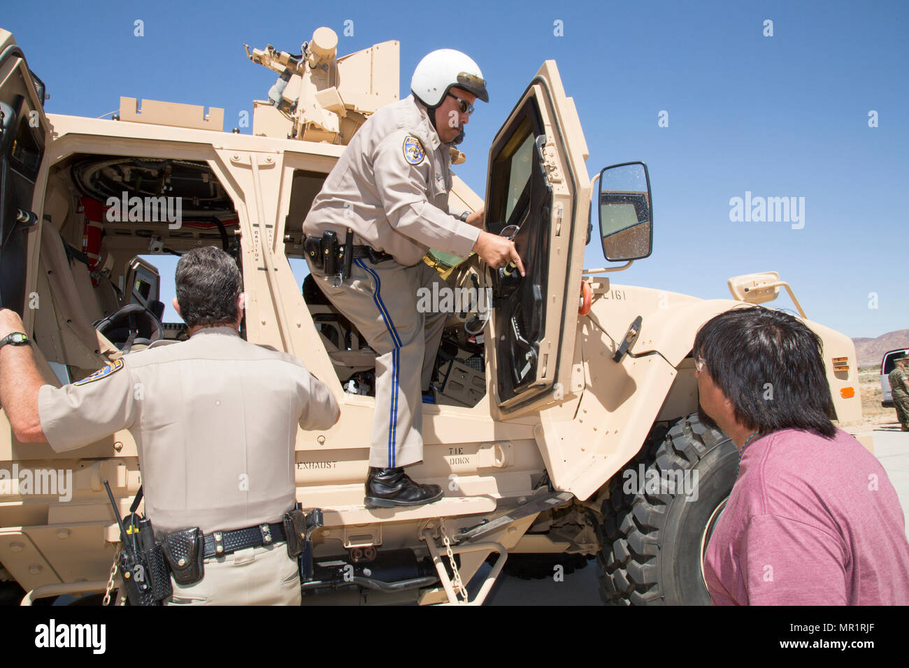 (Sinistra) California Highway Patrol Officer James Anderson, Barstow CHP stazione; e il cap. John Tyler, commander, Barstow CHP stazione; indossa un casco come parte del suo equipaggiamento protettivo personale, salire in una miniera agguato resistente All-Terrain protetti da veicolo a veicolo cingolato Area di test a bordo di impianto di produzione Barstow, Marine Depot comando di manutenzione, sul Yermo allegato del Marine Corps base logistica Barstow, California, 28 aprile. Kenny Phillips, sovrintendente di produzione, M-linea ATV, Stand by per assistere come i funzionari di polizia prendere un tour dell'impianto. Foto Stock