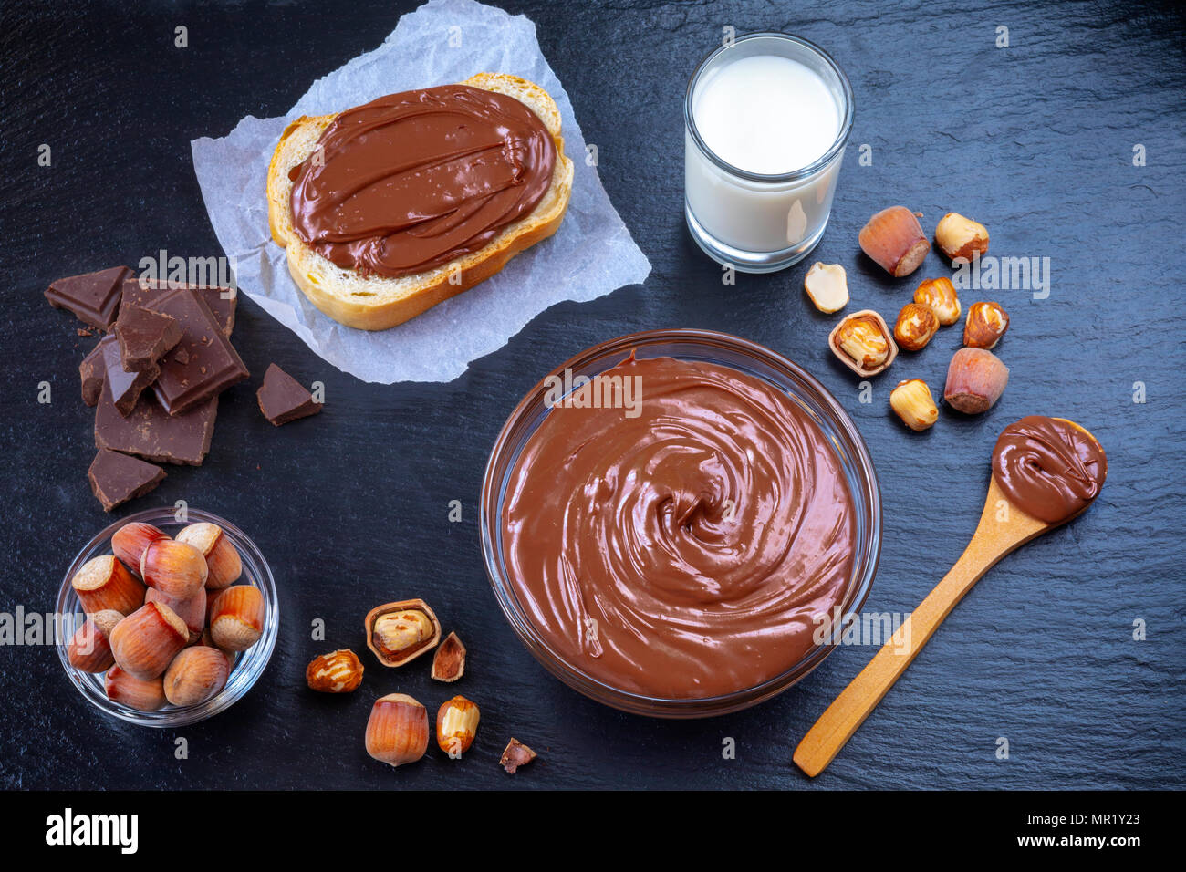 Fetta di pane con il diffondersi di crema di cioccolato e nocciole sulla tavola nera. Serve una deliziosa colazione concetto. Foto Stock