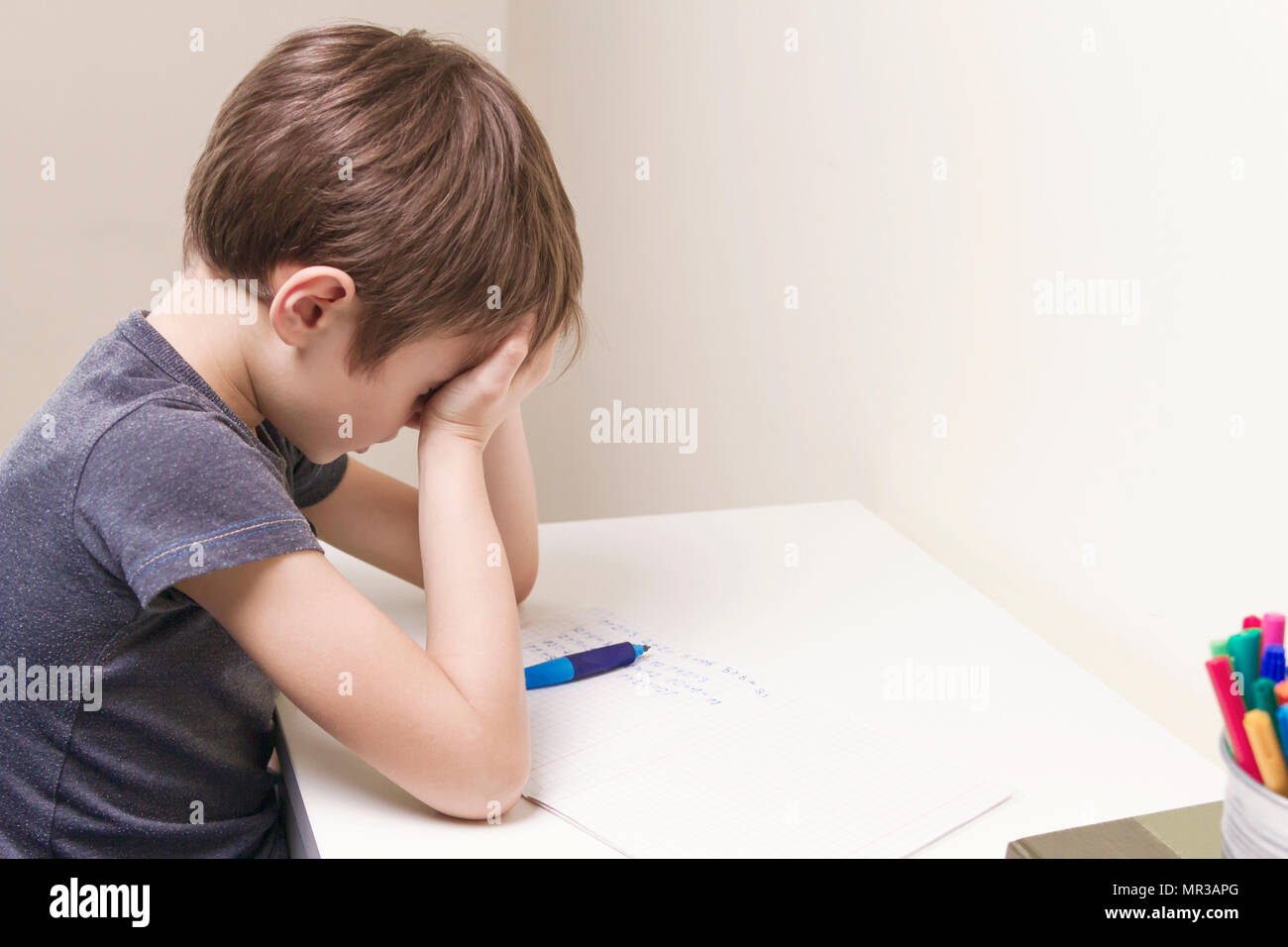 Stanco bambino facendo i compiti a casa. Il ragazzo stufi e si copre il viso con le mani. Istruzione, scuola, difficoltà di apprendimento concetto Foto Stock