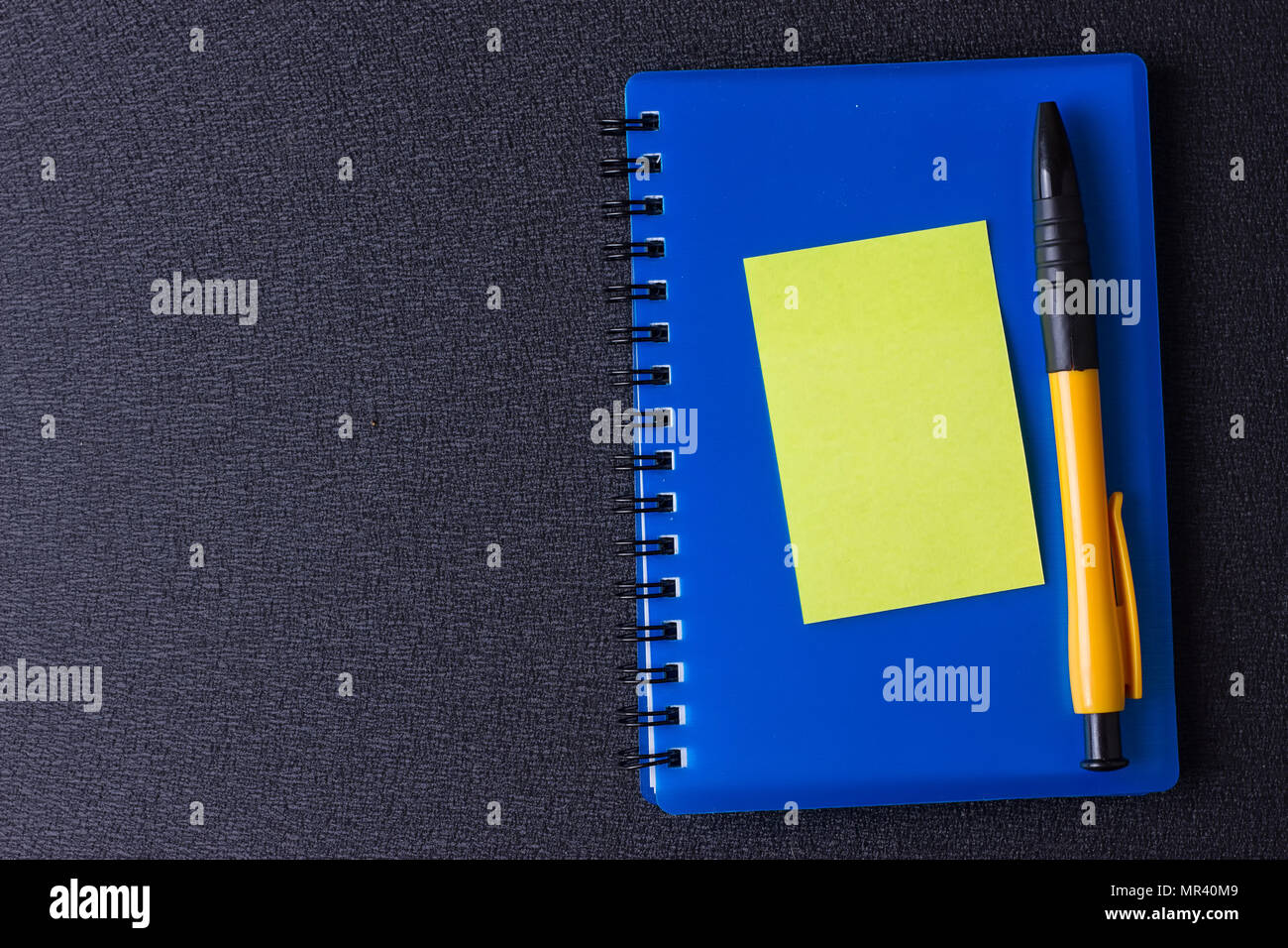 Il blocco note di blu con multi-adesivi colorati e penna su uno sfondo nero Foto Stock