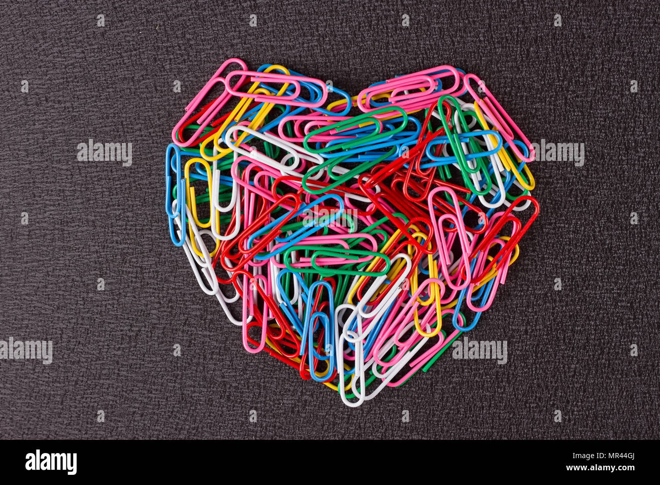 Varietà di colore clip di carta disposti in forma di cuore su sfondo nero. Foto Stock