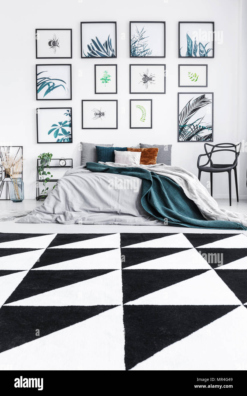 Foto reale di un letto in piedi in una camera da letto con interni in bianco e nero, triangolo rug e dipinti su una parete Foto Stock