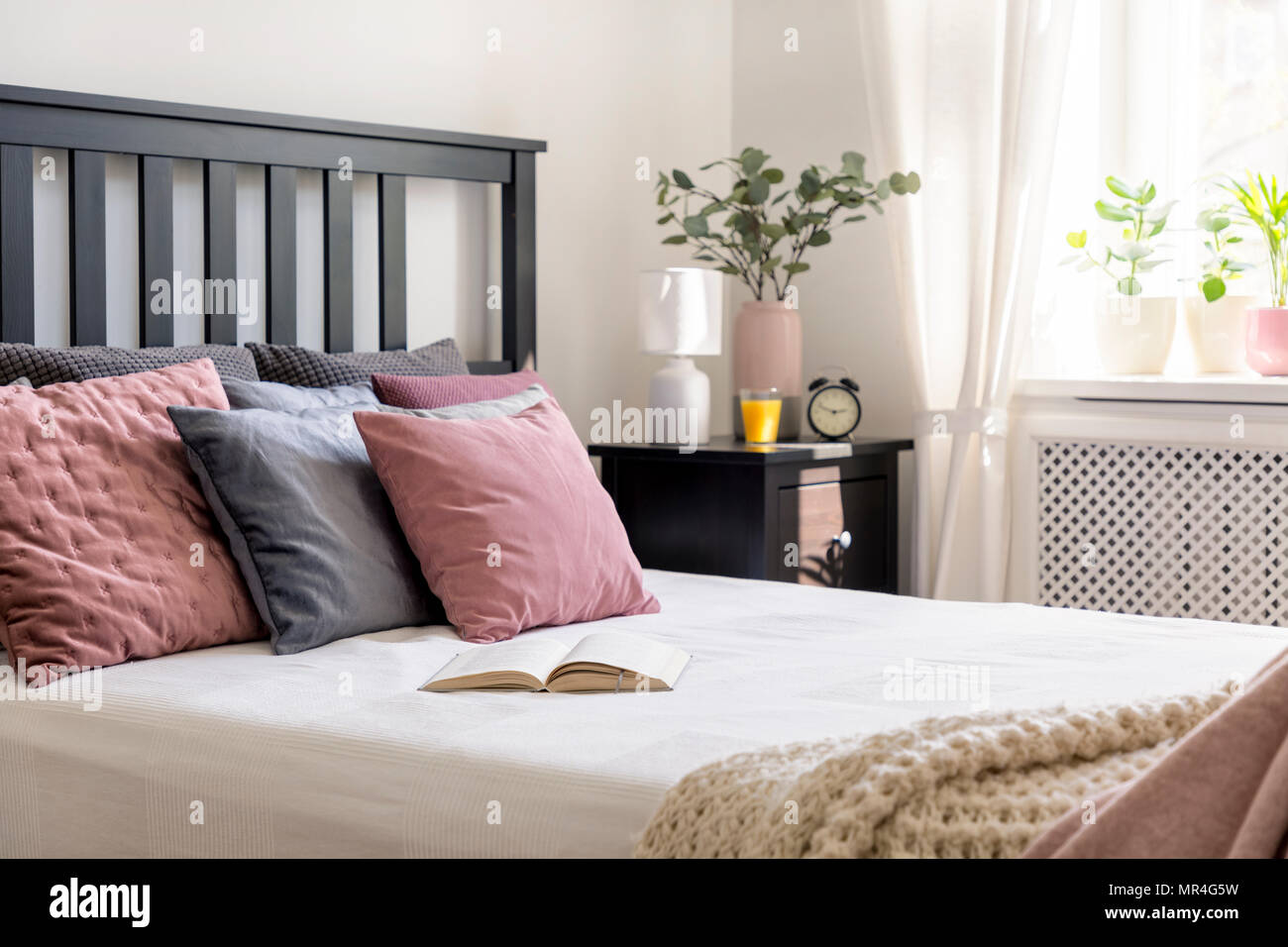 Close-up su di un libro e di rosa e grigio cuscino sul letto in camera da letto accogliente interno con impianto. Foto reale Foto Stock