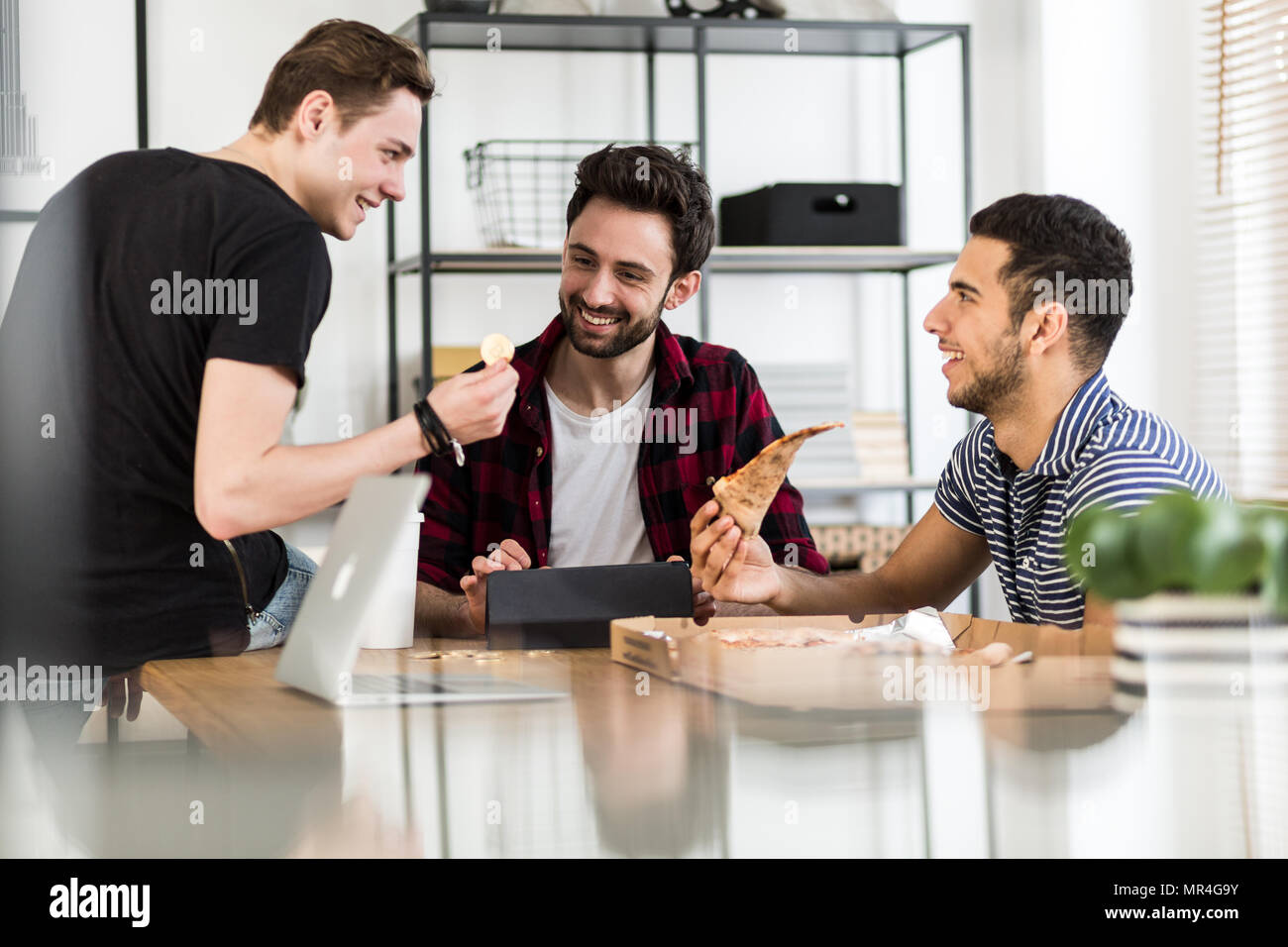 Sorridendo gli amici di mangiare la pizza e parlando di cryptocurrency digitale Foto Stock