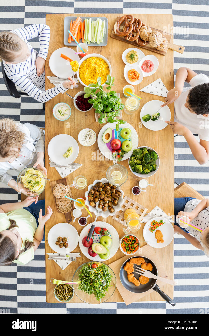 Vista dall'alto sulla tavola con il cibo. Gruppo di bambini mangiare sano la cena con verdure Foto Stock