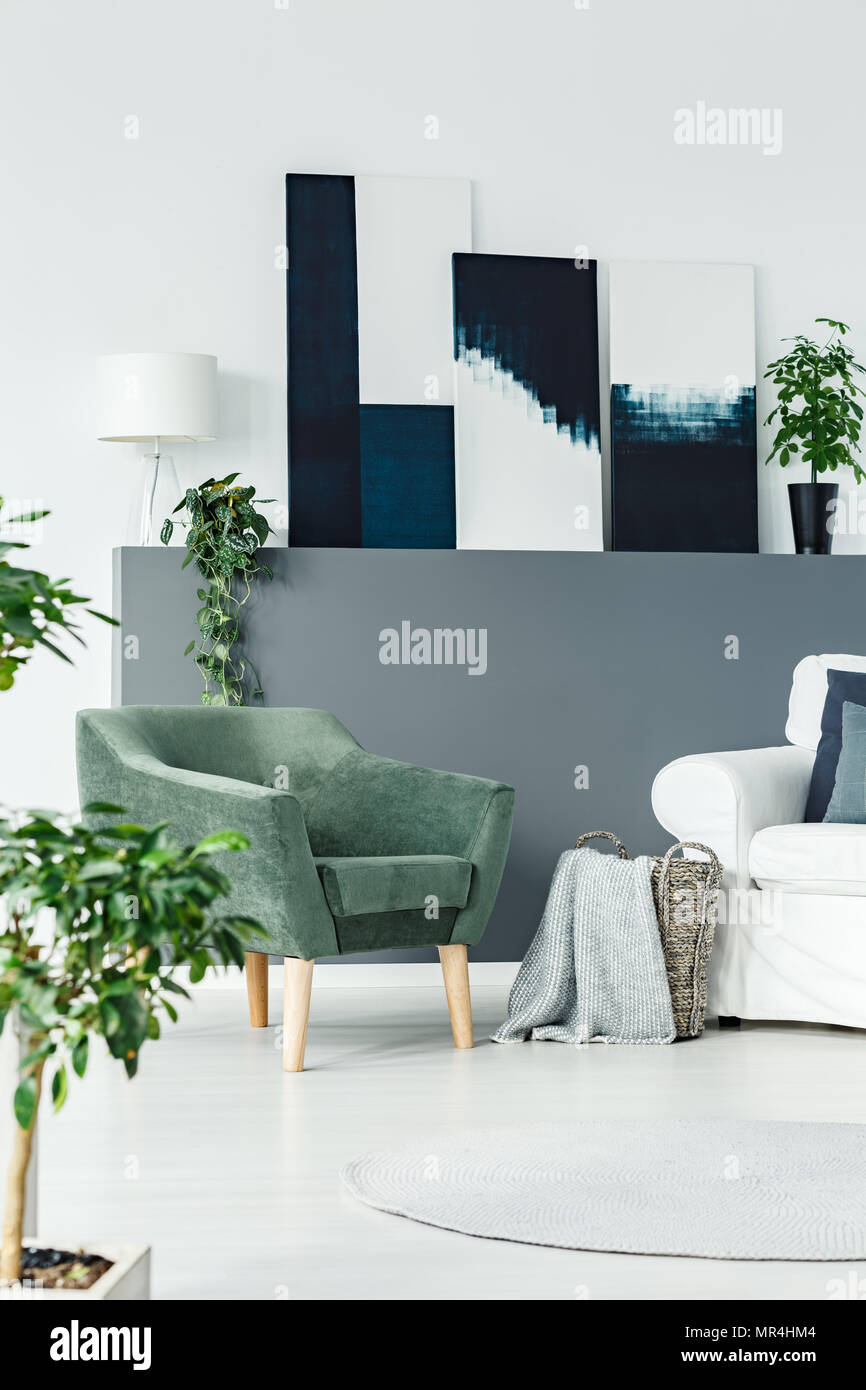 Poltrona verde in piedi in bianco salotto interno con piante fresche e dipinti di arte moderna Foto Stock