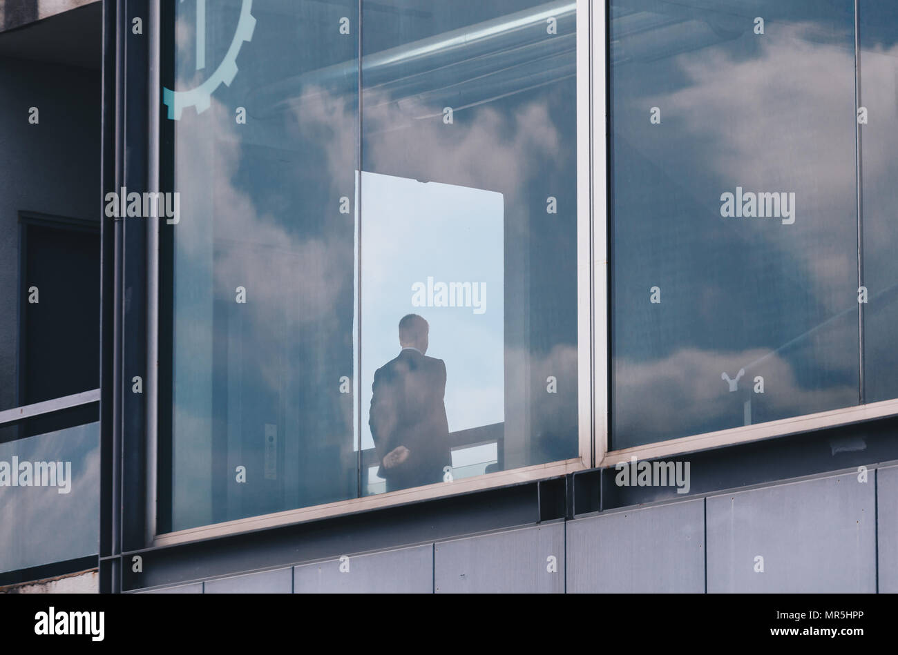 Business man guardando sopra la finestra in un edificio moderno con il riflesso del Cielo e nubi in Windows Foto Stock