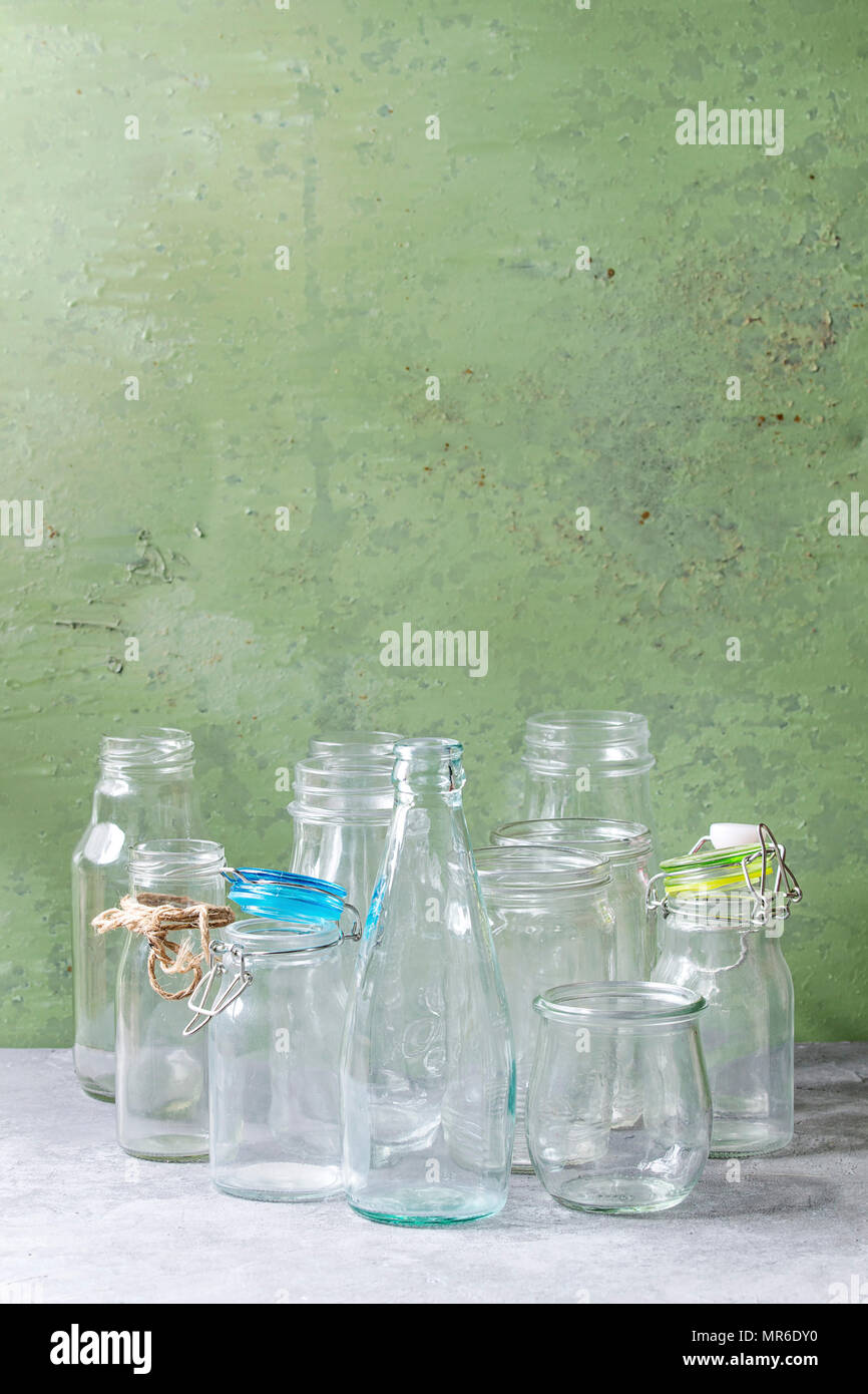 Varietà di diversa forma vuoto aperto le bottiglie di vetro con e senza coperchi permanente sulla tabella grigia con parete verde come sfondo. Foto Stock