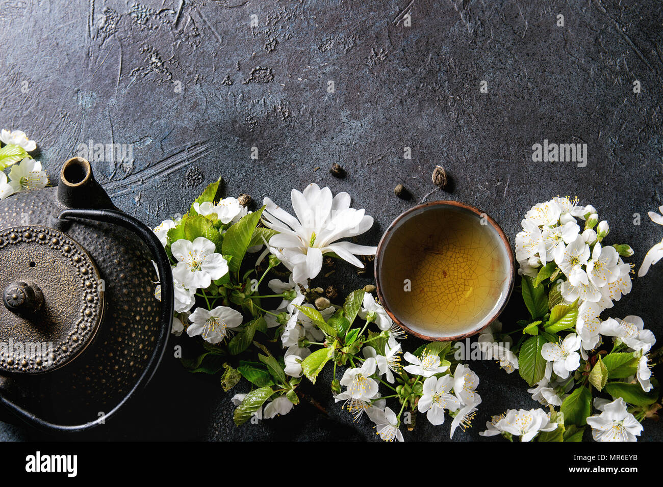 Ceramica tradizionale tazza di acqua calda tè verde con ferro nero teiera,  molla fiori bianco magnolia e ciliegio rami fioriti su blu scuro texture bac  Foto stock - Alamy
