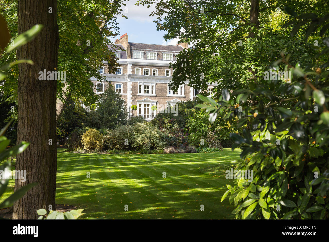 Una frondosa piazza con giardino nel quartiere di Kensington, Londra, Regno Unito, su un giorno di estate con stucco terrazzati townhouses in background Foto Stock