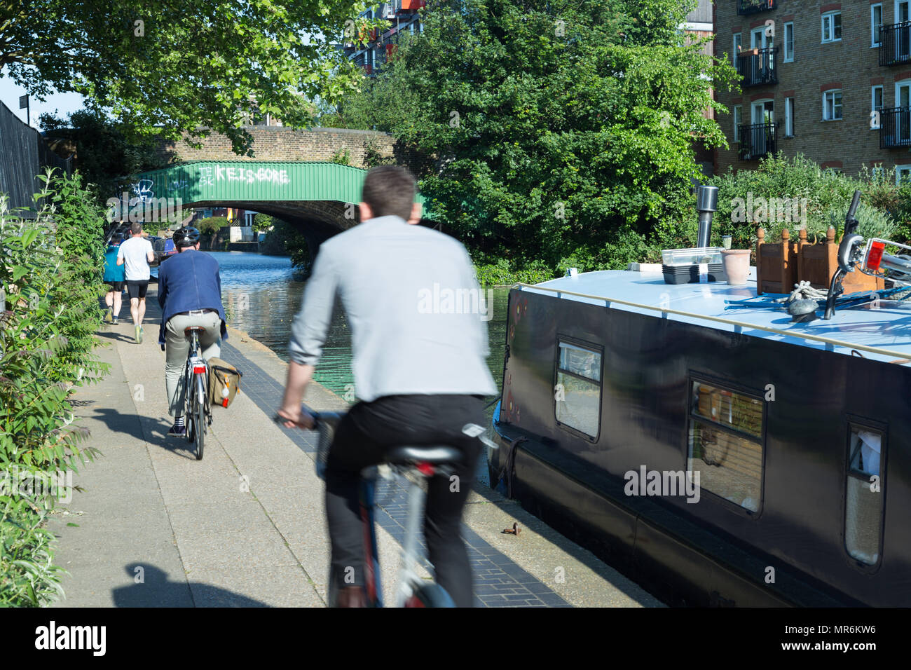 Per gli amanti del jogging jogging e pendolari in bicicletta a Rush Hour passato un narrowboat sul Regent's Canal in Haggerston, East London, Regno Unito, su una serata primaverile Foto Stock