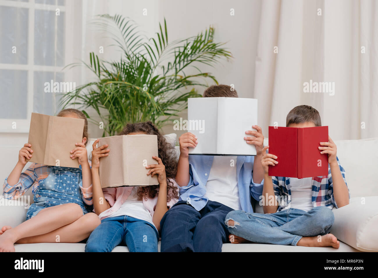 Oscurata vista dei bambini facce di copertura con libri durante la lettura a casa Foto Stock