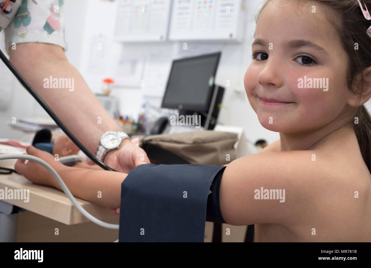 Bambina essendo dando del test della pressione del sangue medico. Lei è sorridente alla fotocamera Foto Stock