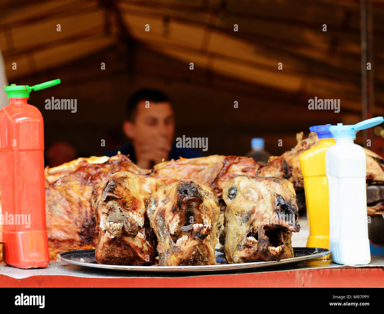Teste di agnello tagliati da agnelli arrosto in precedenza a uno sputo. In una sfocata che circonda, le bottiglie di plastica per un ketchup, senape e la maionese. Foto Stock