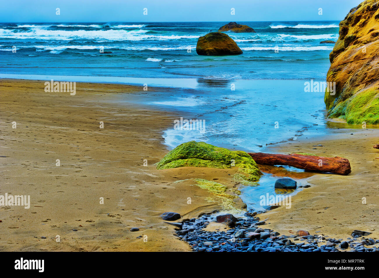 Oregon spiaggia costiere dove un piccolo torrente conduce lo sguardo verso le onde dell'Oceano Pacifico. Rocce intercotidali diventando circondano dalla marea. Foto Stock
