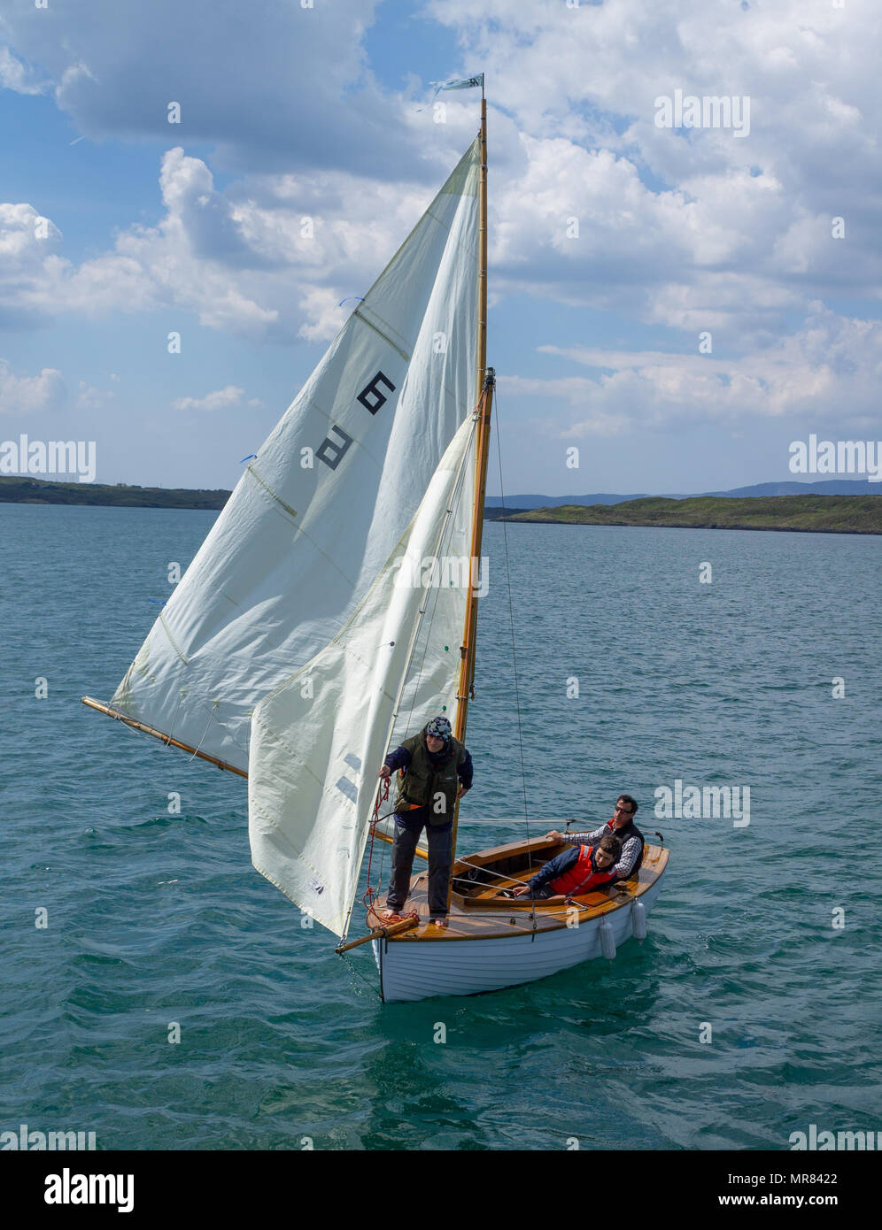 Il clinker costruito in legno dinghy in barca a vela o barca essendo navigato nel porto di Baltimora, Irlanda da un giovane godendo il tempo in estate. Foto Stock