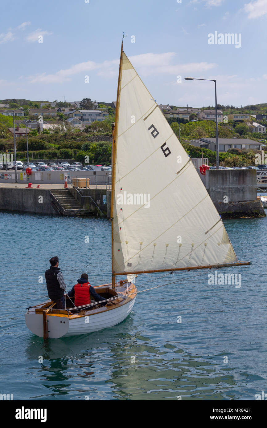 Il clinker costruito in legno dinghy in barca a vela o barca essendo navigato nel porto di Baltimora, Irlanda da un giovane godendo il tempo in estate. Foto Stock