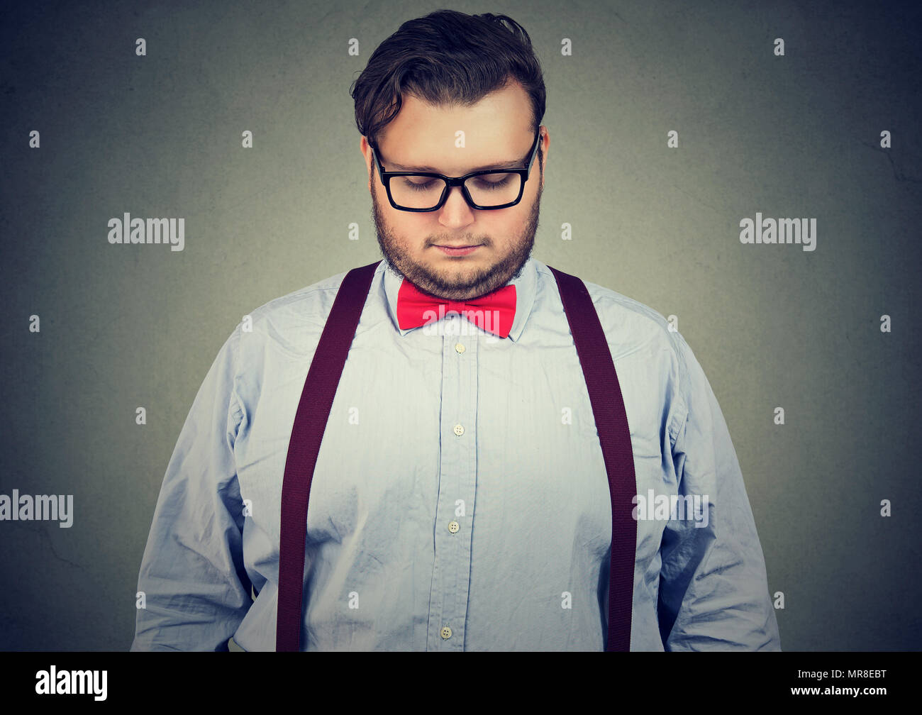 Chubby eccentrico uomo in tempo di prua con gli occhiali e tenendo testa giù nel dolore. Foto Stock