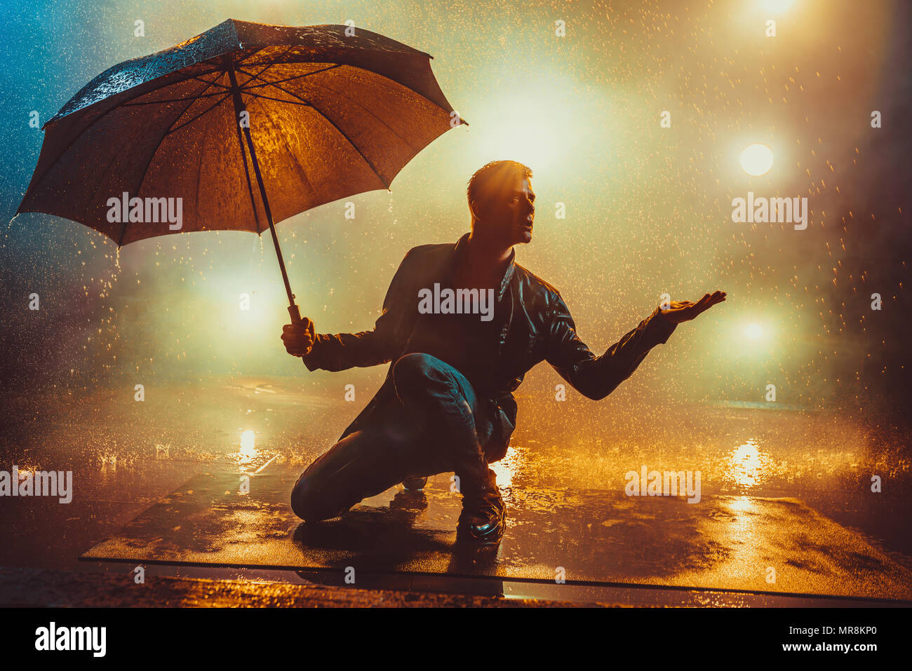 Giovani strano Uomo con ombrello sotto la pioggia. Luci brillanti sullo sfondo. Foto Stock