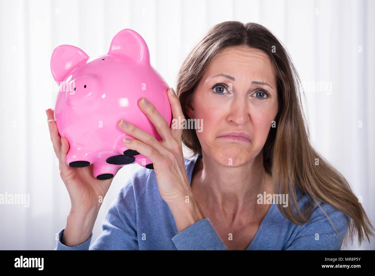 Close-up di donna infelice Holding Piggybank contro di persiane Foto Stock