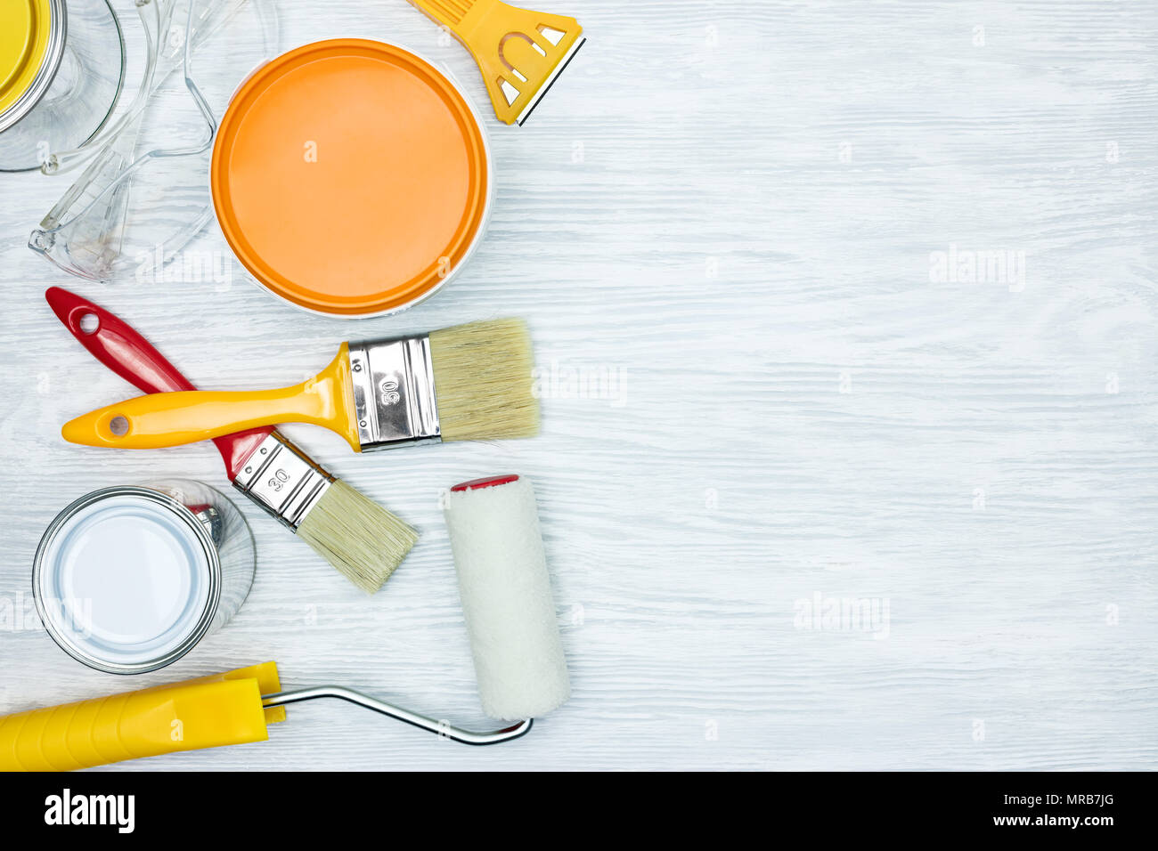 Pennelli, rulli, coltello, occhiali di protezione e la vernice può su legno sfondo grigio vista piana Foto Stock