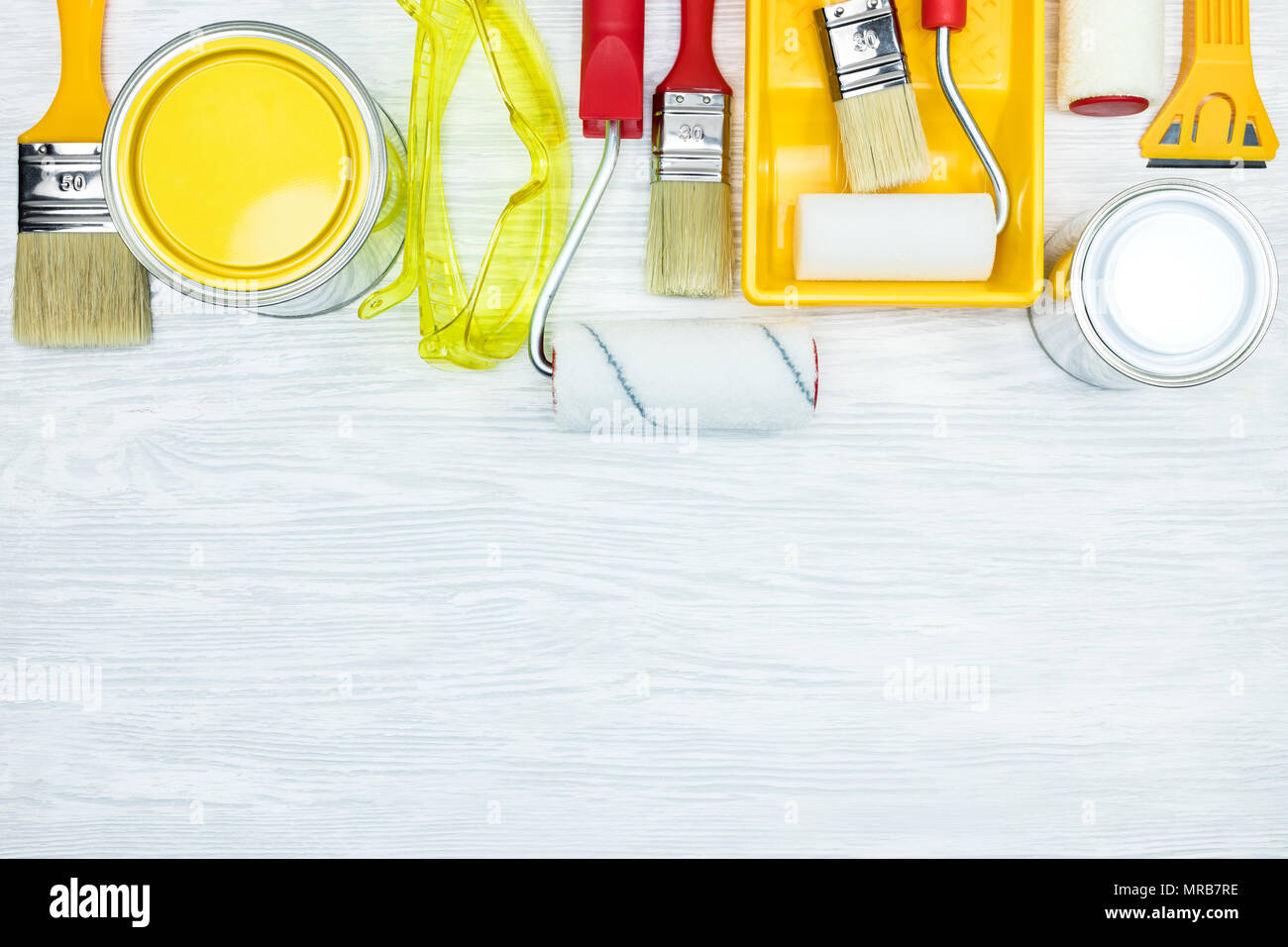 Vari pennelli, vernice, occhiali protettivi, Rulli vassoio di vernice, coltello da stucco grigio sulla superficie di legno vista piana Foto Stock
