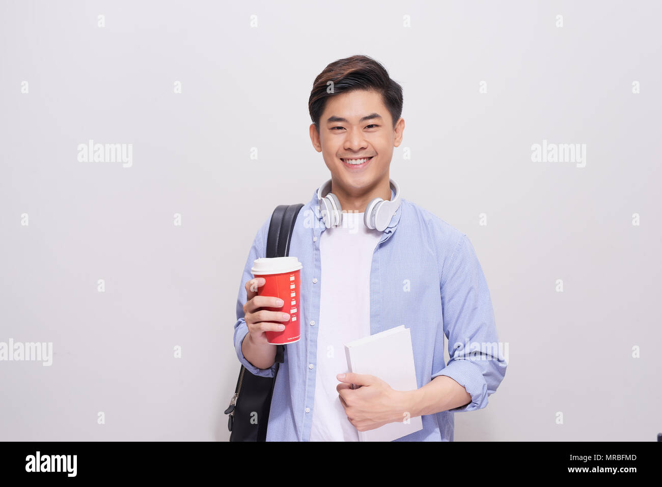 Pausa caffè. Positivo bello studente di scuola superiore tenendo un smartphone e di bere il caffè in piedi contro il muro grigio Foto Stock