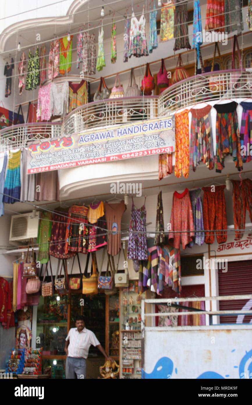 Uomo indiano al di fuori del turista negozio di abbigliamento, con Colorati luminosamente Abbigliamento e borse di riagganciare, Varanasi, India Foto Stock