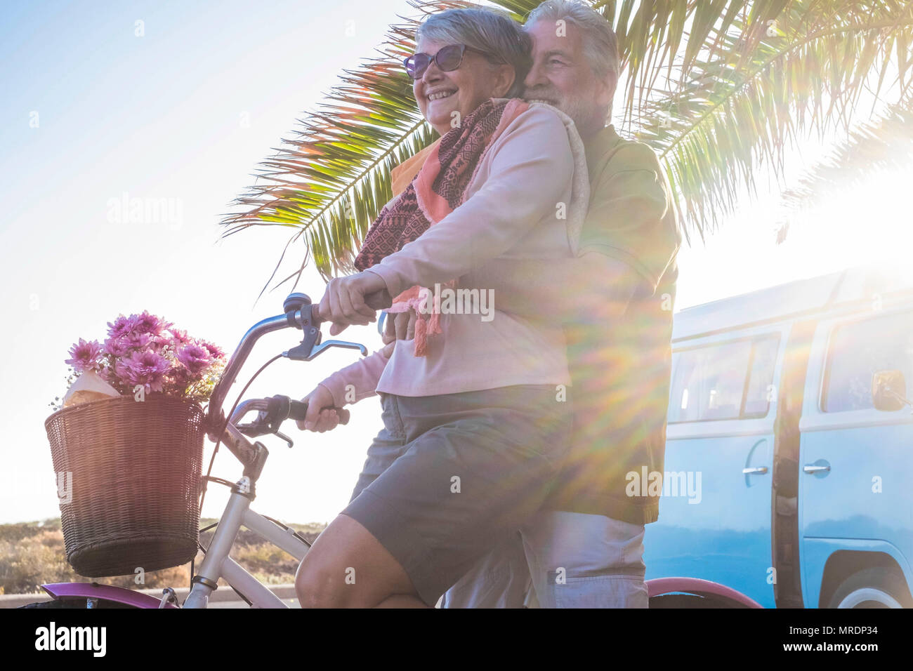 Bella bella coppia di anziani nonni andando insieme su una bicicletta all'aperto in un luogo tropicale. vecchio blu vintage van in background. happine Foto Stock