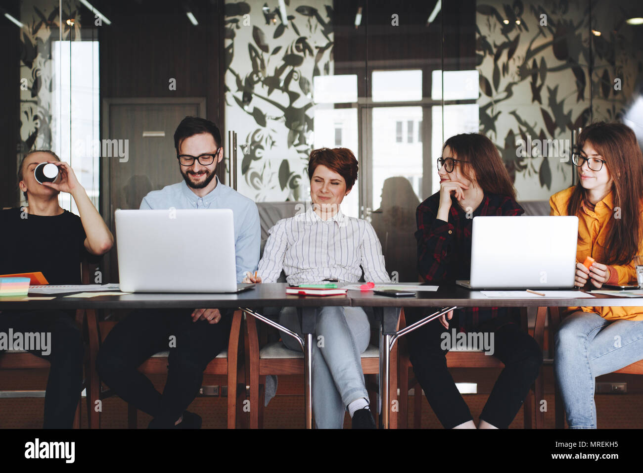 Gioioso team di collaboratori che lavorano insieme in un moderno loft spazio sulla tavola di legno con moderni laptop. Il lavoro di squadra sul nuovo sturt fino Foto Stock