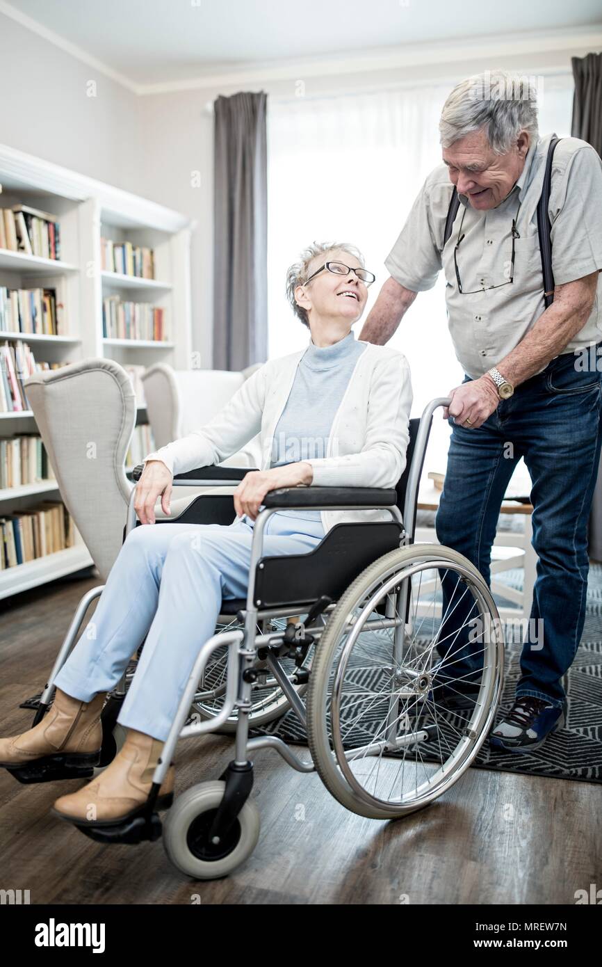 Senior donna in carrozzella guardando l uomo e sorridente. Foto Stock