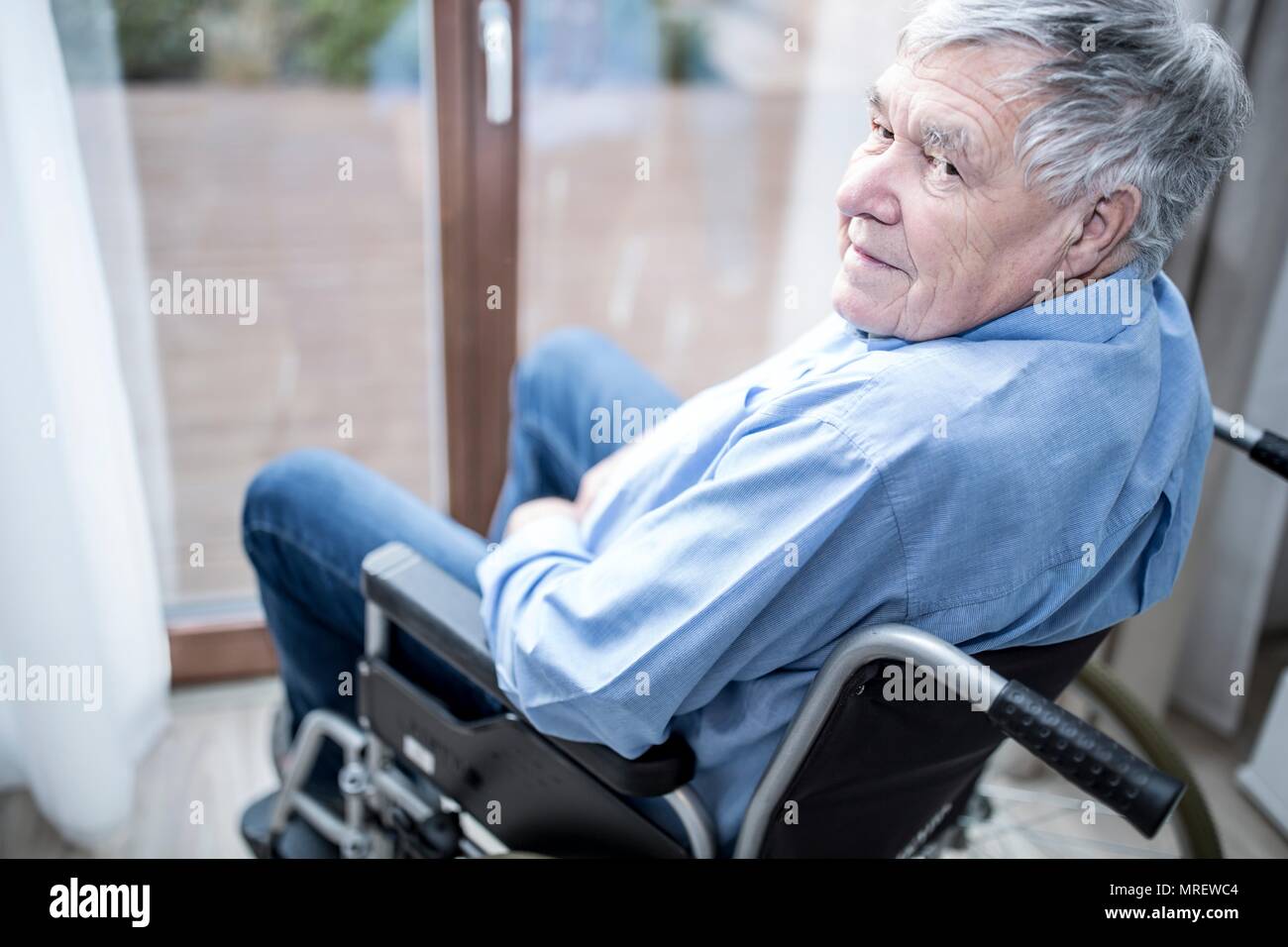 Senior uomo in sedia a rotelle dalla finestra in casa di cura. Foto Stock