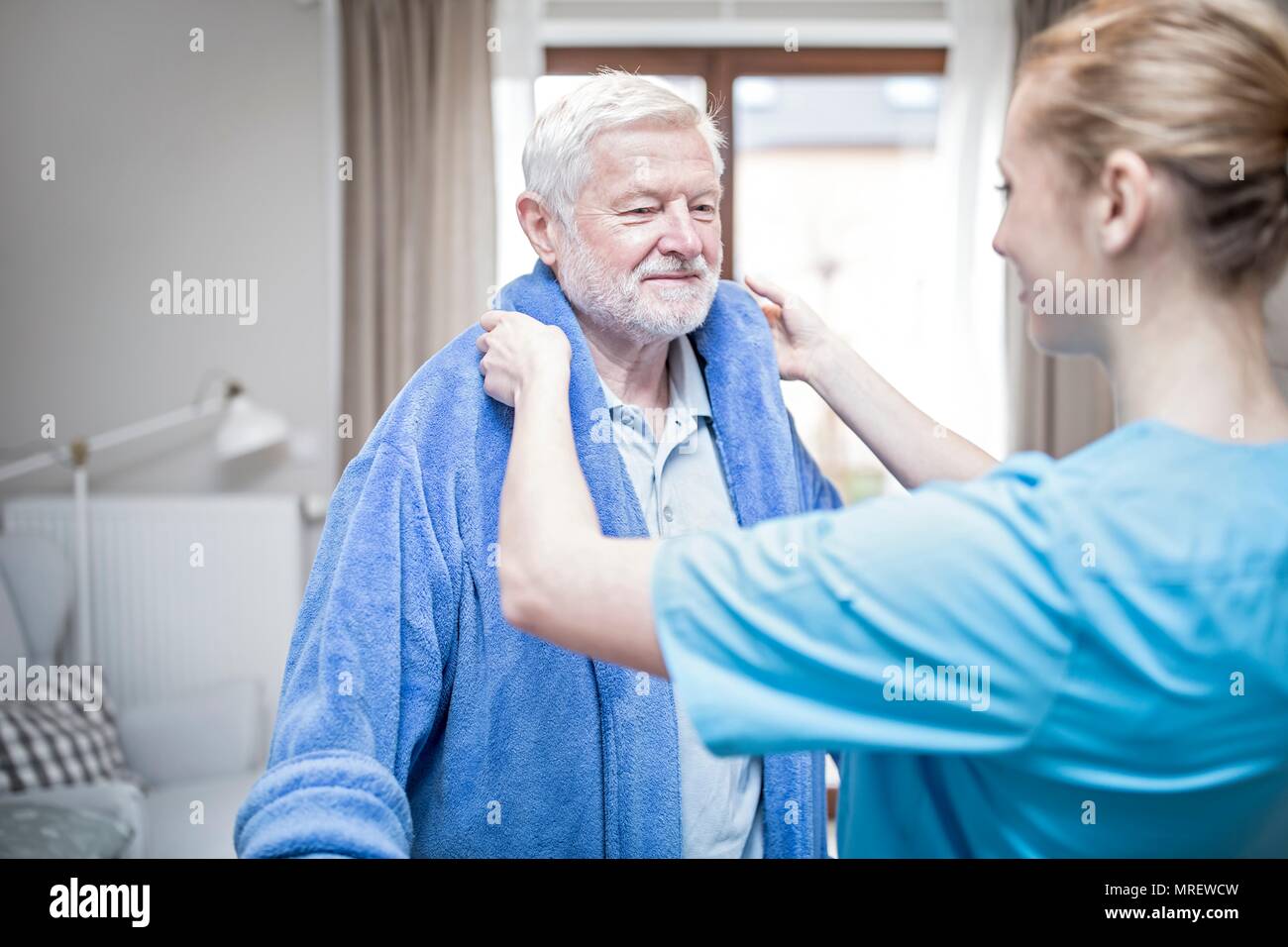 Lavoratore di cura senior aiuta l uomo a mettere in vestaglia. Foto Stock