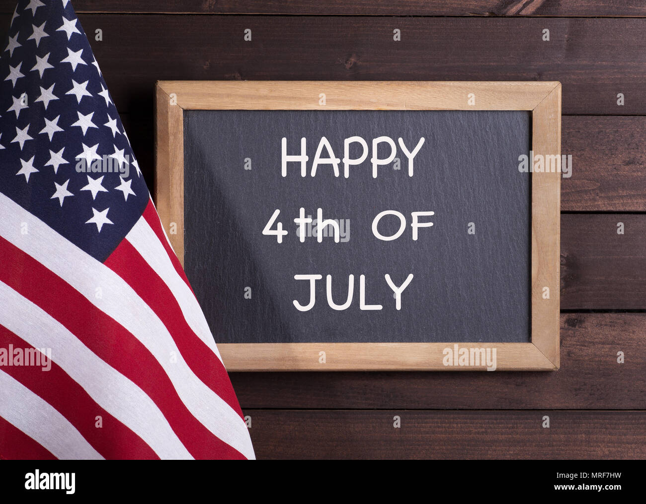 Bandiera americana e felice del 4 luglio scritto su una lavagna su un rustico sfondo di legno Foto Stock