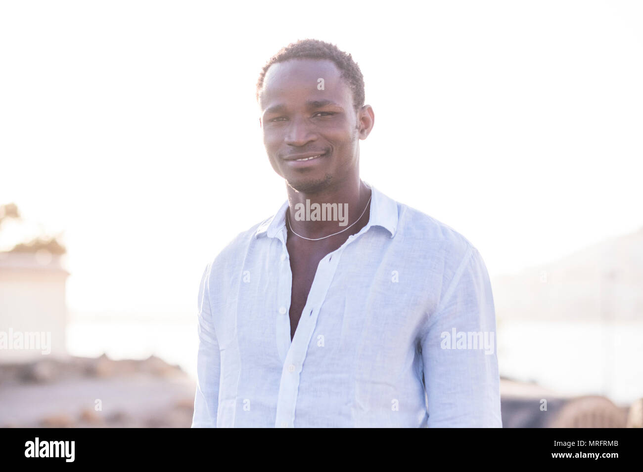 Moda bella gara nera modello africana uomo con una camicia bianca e bella faccia guardare la fotocamera. sfondo sfocato outdoot ubicazione sfocato. Foto Stock