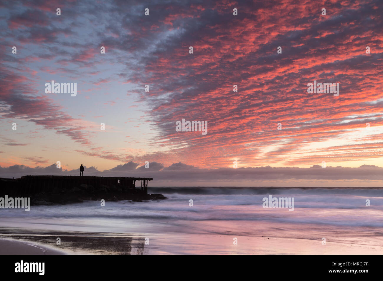 Un uomo si erge su un molo di decadimento nel timore di un vibrante sunset, creando un netto contrasto tra la Città Santa Monica Bay e la bellezza naturale di Los un Foto Stock