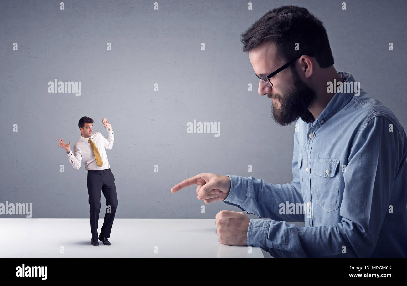 Giovane imprenditore professionale essendo arrabbiato con un altro imprenditore in miniatura di fronte a uno sfondo grigio Foto Stock
