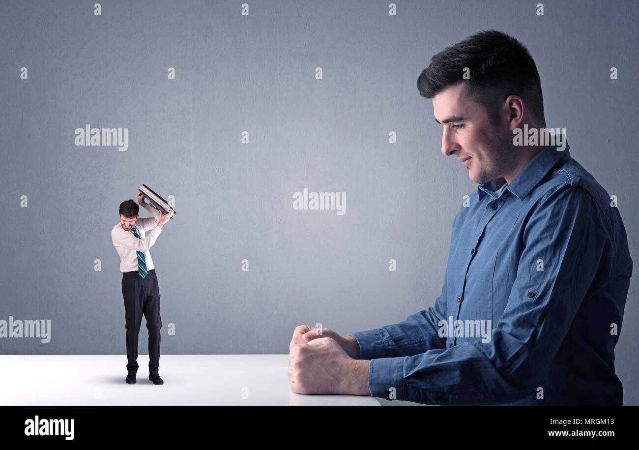 Giovane imprenditore professionale essendo arrabbiato con un altro imprenditore in miniatura nella parte anteriore di un bluastro sfondo grigio Foto Stock