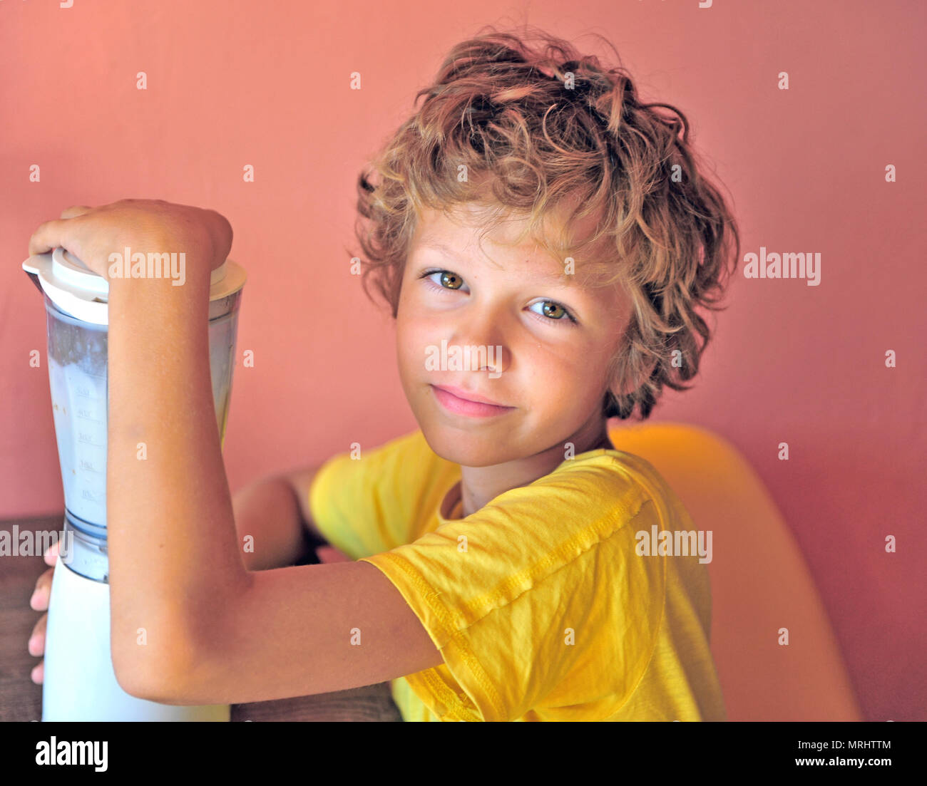 Portrair di un ragazzo felice rendendo milk shake per se stesso seduto alla cucina, adorabili caucasian capretto con shaggy capelli Foto Stock