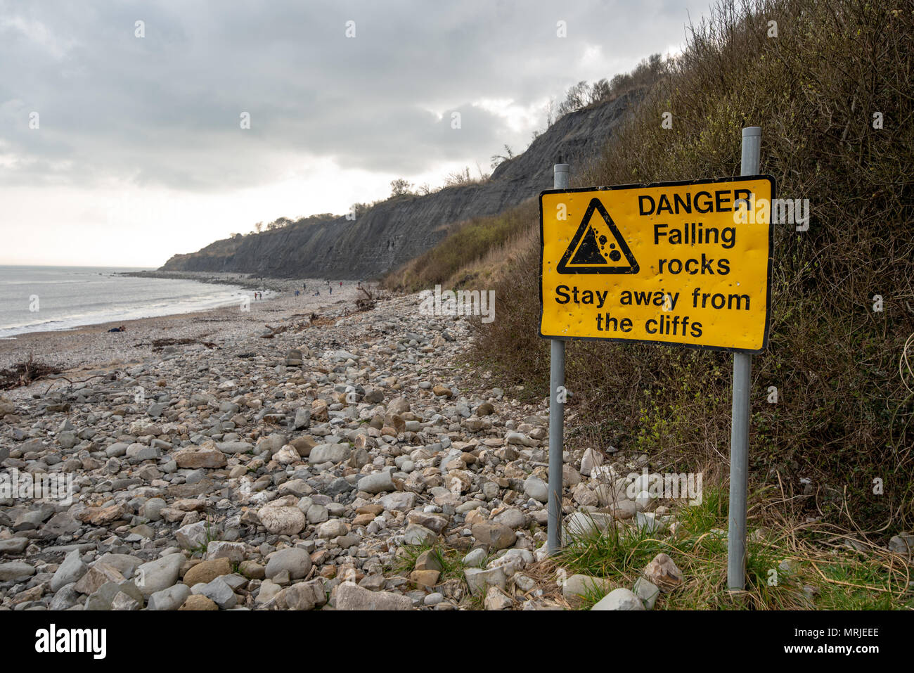 Un giallo luminoso segno di Pericolo attenzione di caduta di rocce dalle scogliere lungo il Lyme Regis spiaggia fossile, Dorset, Regno Unito. Foto Stock