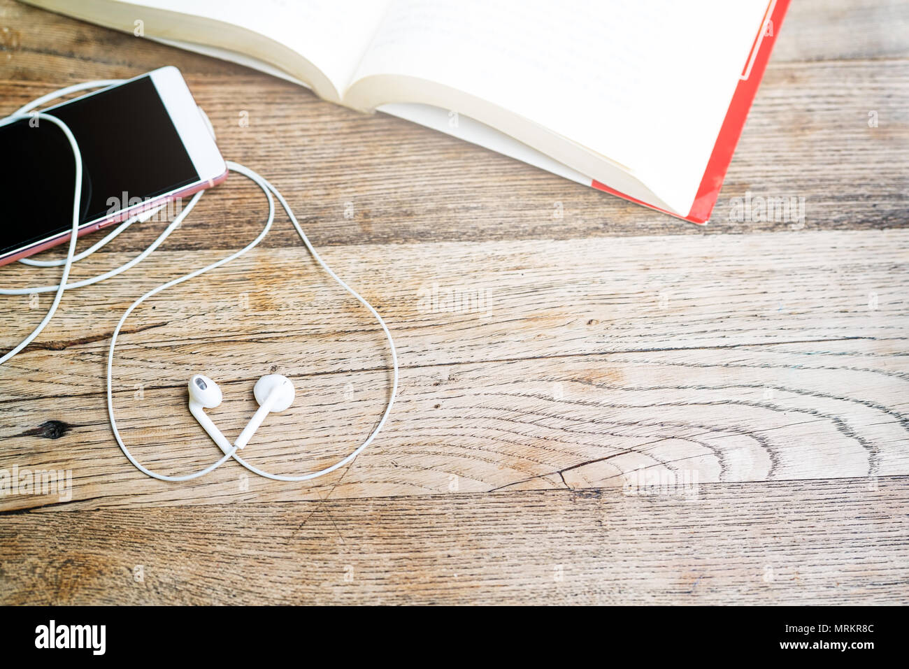 Cuore bianco forma auricolare con lo smartphone e un libro aperto sul tavolo di lavoro vista superiore con spazio di copia Foto Stock