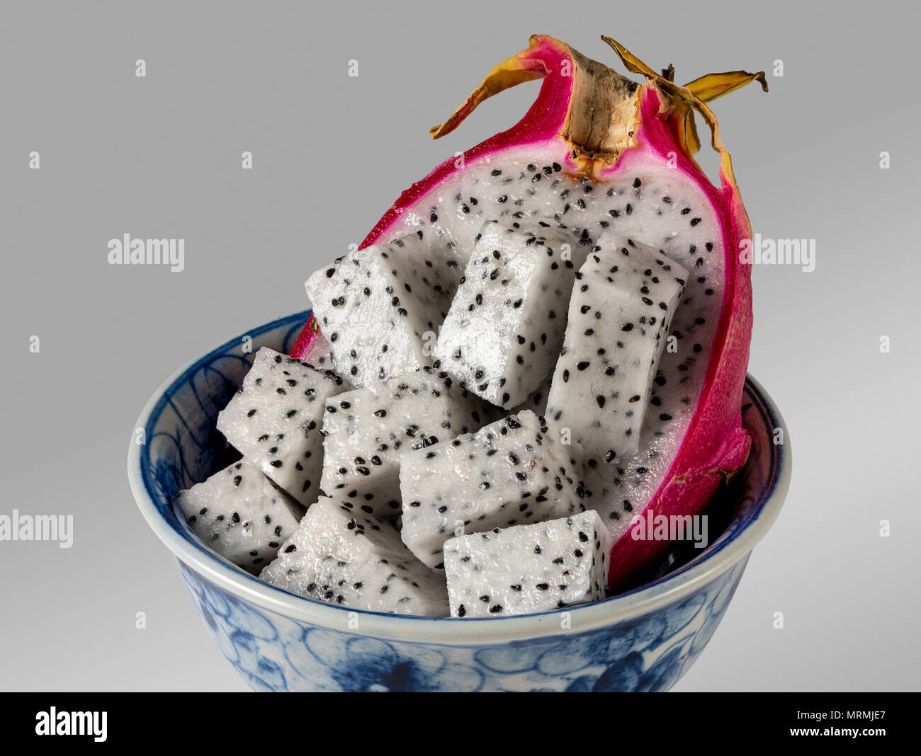 Dragon frutta tagliata a metà in una ciotola blu contro uno sfondo grigio Foto Stock