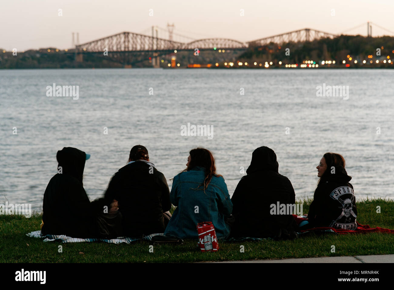 Un gruppo di amici seduti lungo il fiume San Lorenzo in Quebec City, con il famoso Pont de Quebec oltre Foto Stock