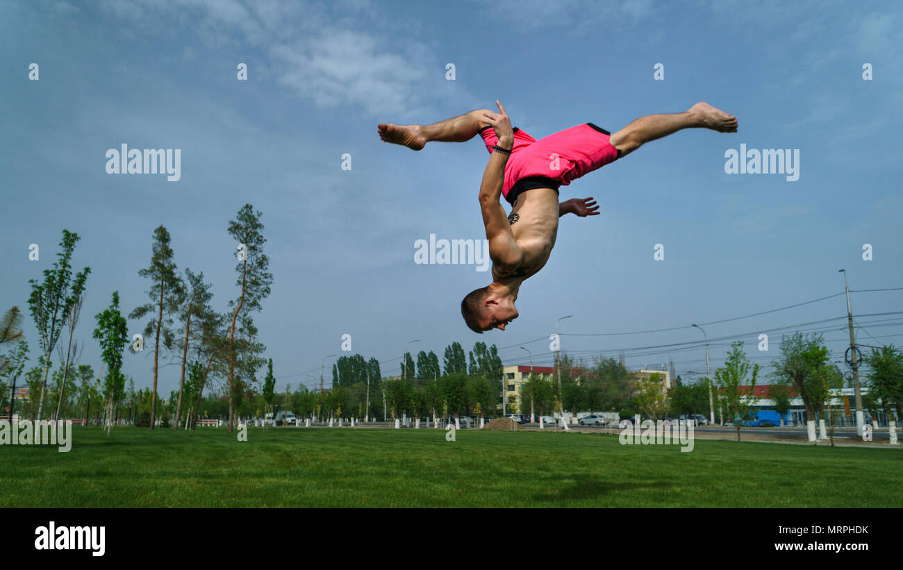 Tricking sul prato nel parco. L'uomo flips indietro e kick. Arti marziali e parkour. Allenamento di strada. Foto Stock