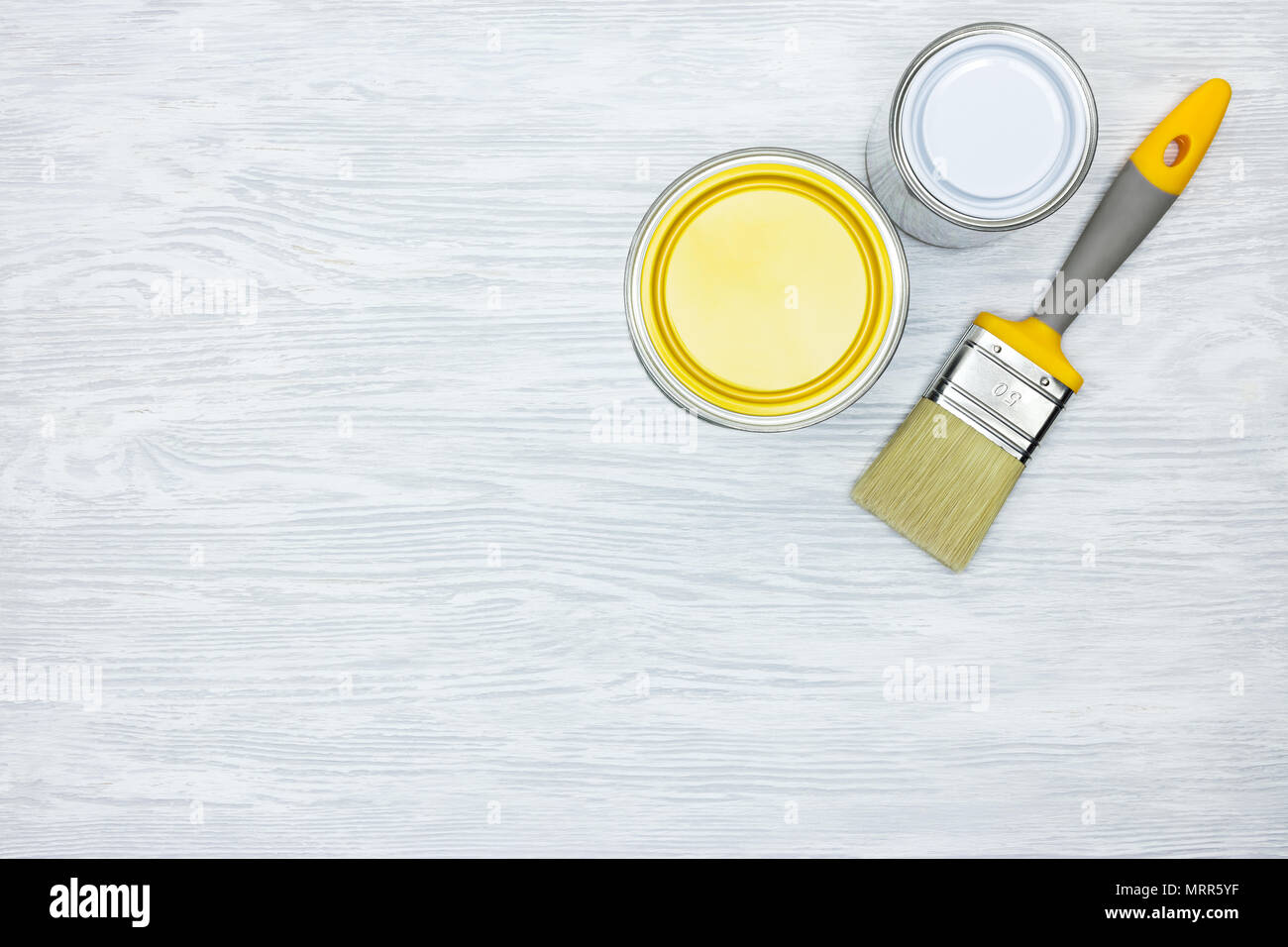 Le lattine con il bianco e il giallo e il pennello sul grigio Sfondo di legno Foto Stock