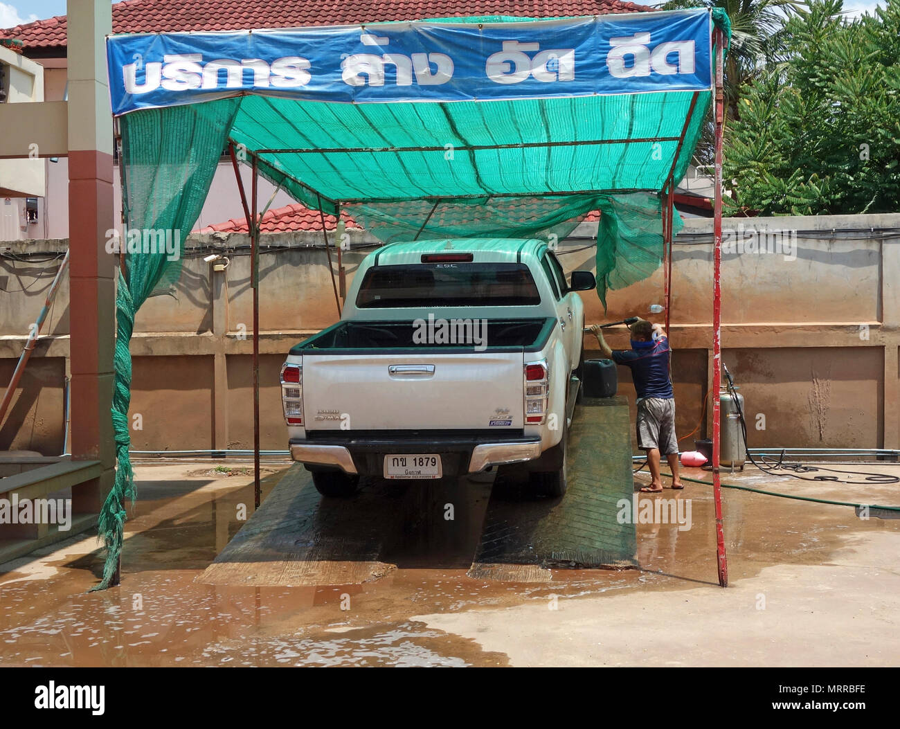 Urban outdoor car wash con operaio di lavaggio di un raccoglitore bianco carrello utilizzando un azionato manualmente il dispositivo di spruzzo, Udon Thani, Isaan, Thailandia Foto Stock