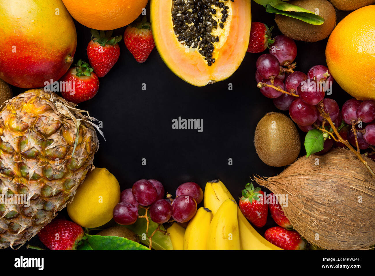 Telaio con copia spazio dal fresco tropicale e l'estate Frutta di stagione Ananas Papaia Mango Coconut Arance Kiwi banane Limoni Pompelmi e pomeli su nero Ba Foto Stock