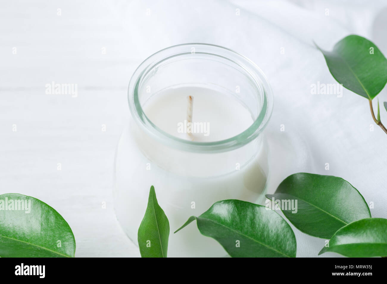 Candela bianca in un barattolo di vetro fresco rami di albero con tenera foglie verdi su legno e biancheria da letto di cotone tessuto sfondo. Spa Wellness per la cura del corpo P di meditazione Foto Stock