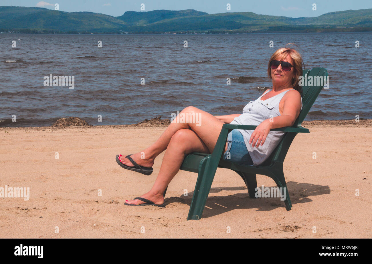Donna in pensione in vacanza seduto alla spiaggia Lago Maskinonge St-Gabriel-de-Brandon Québec Canada Foto Stock